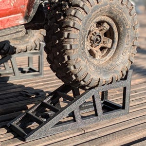 Pode incluir: Rampa de metal preto para um carro ou caminhão de brinquedo. A rampa tem uma superfície texturizada e é projetada para levantar as rodas do veículo.