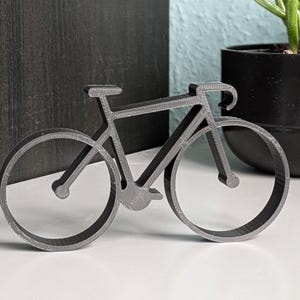Puede incluir: Una silueta de bicicleta de metal negro, un artículo de decoración del hogar popular.