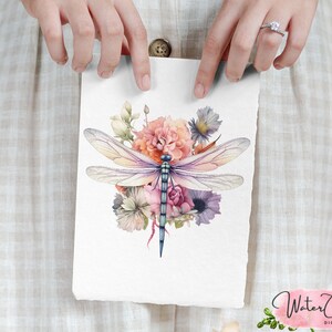 May include: Watercolor illustration of a dragonfly with blue and purple wings, surrounded by a bouquet of pink, white, and orange flowers.