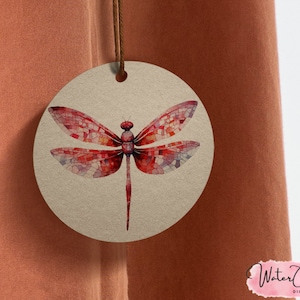 May include: A round, brown tag with a red dragonfly illustration. The dragonfly's wings are made of mosaic-like pieces of red, pink, and white.