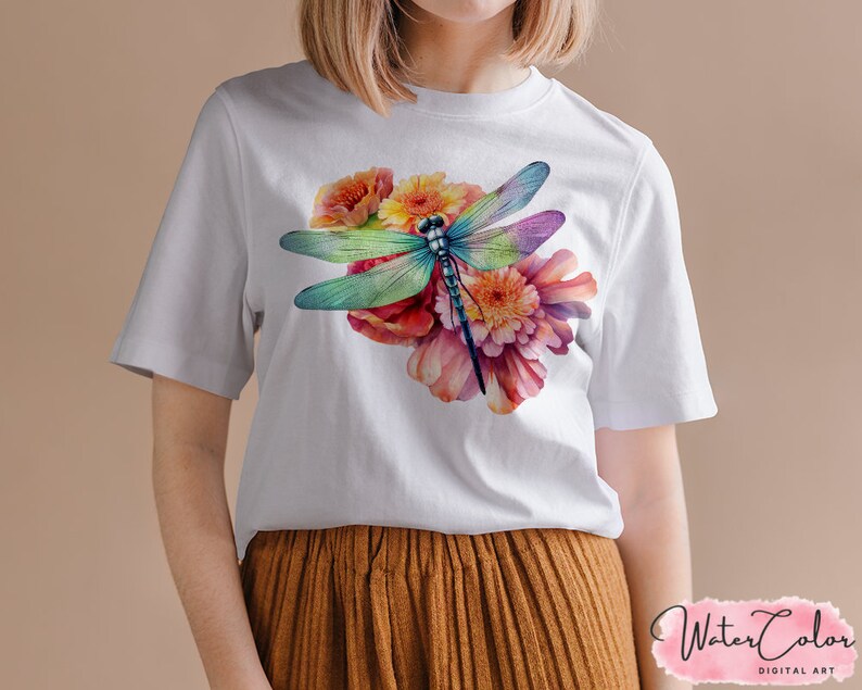 May include: White t-shirt with a watercolor design of a dragonfly and flowers. The dragonfly is blue, green, and purple, and the flowers are pink, orange, and yellow.