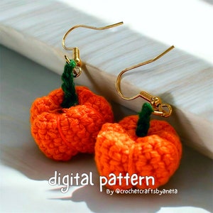 May include: A pair of handmade crochet pumpkin earrings. The earrings feature small, orange pumpkins with green stems and gold-coloured ear wires. The text "digital pattern" and the seller's name are visible.