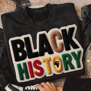 Può includere: Felpa nera girocollo con una grande grafica colorata "BLACK HISTORY". Il design include una silhouette nera dell'Africa. Sono visibili anche una giacca di jeans patchwork e pantaloni neri. Il testo "WAIT4IT DESIGN ORIGINAL DESIGNER" è in basso.