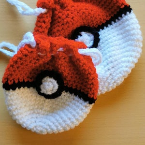 May include: Two crocheted Pokeball drawstring bags, one red and white and one red and white with the red portion folded over the white portion.