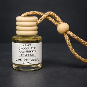 May include: A clear glass car diffuser bottle with a wooden cap and a braided rope for hanging. The label reads "White Chocolate Raspberry Truffle Car Diffuser 10 ml."