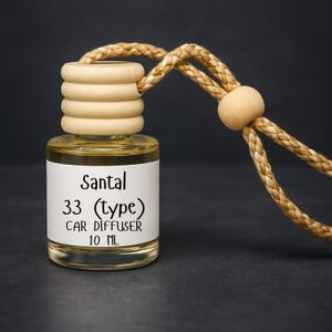 May include: A clear glass car air freshener bottle with a wooden cap and a braided rope. The label reads "Santal 33 (type) CAR DIFFUSER 10 ML". The liquid inside is amber-colored. The background is dark gray.