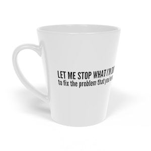 Op de afbeelding: Witte keramische latte-mok met zwarte tekst die luidt: "Laat me stoppen met wat ik doe om het probleem op te lossen dat je hebt veroorzaakt."