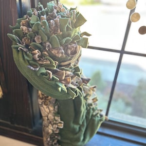 May include: A fabric snuffle mat featuring a base of solid dark green fleece with numerous strips of green and camouflage-patterned fleece tied to the surface, creating a dense, textured, and layered appearance for this interactive pet accessory.
