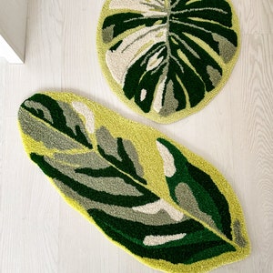 May include: Two green and white leaf-shaped rugs with a textured, fuzzy surface. The rugs are on a light wood floor.
