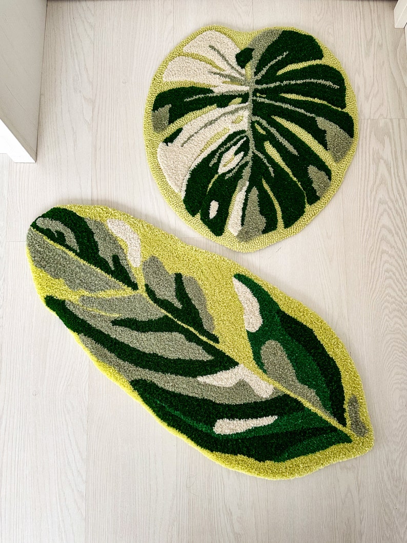 May include: Two green and white leaf-shaped rugs with a textured, fuzzy surface. The rugs are on a light wood floor.