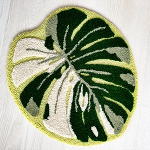 May include: A green and white rug with a large leaf design. The rug is made of a soft, plush material and is perfect for adding a touch of nature to any room.
