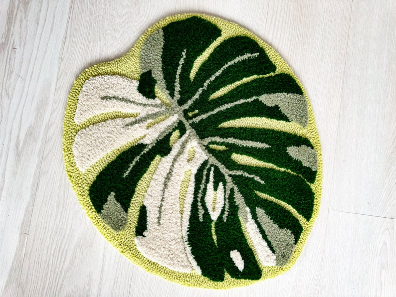May include: A green and white rug with a large leaf design. The rug is made of a soft, plush material and is perfect for adding a touch of nature to any room.