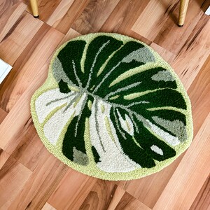 May include: A round, green and white rug with a monstera leaf design. The rug is on a wood floor.