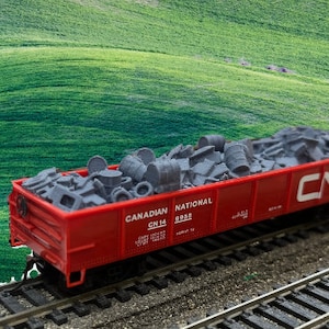 May include: A red model train car with the text "CANADIAN NATIONAL CN 14 8985" on the side. The car is filled with gray metal scraps and is on a model train track.