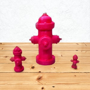 May include: Three pink fire hydrants of different sizes. The largest hydrant is in the center, the smallest is on the right, and the middle-sized hydrant is on the left.