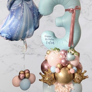 May include: A blue number three balloon with a pink ribbon and the text "Happy Birthday Zaria" is surrounded by a cluster of pastel pink, blue, and gold balloons. A Cinderella character balloon is attached to the bottom of the balloon cluster.