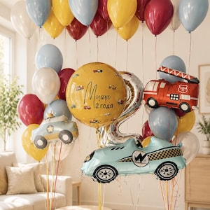 May include: A balloon bouquet featuring a large yellow round balloon with the text "Миша 2 года" and small vehicle illustrations, a silver number 2 balloon, a red fire truck balloon, a light blue race car balloon, and assorted red, yellow, blue, and white balloons.