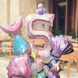 May include: A pink number five balloon with a mermaid tail, seashells, and stars. The balloons are arranged in a bouquet.