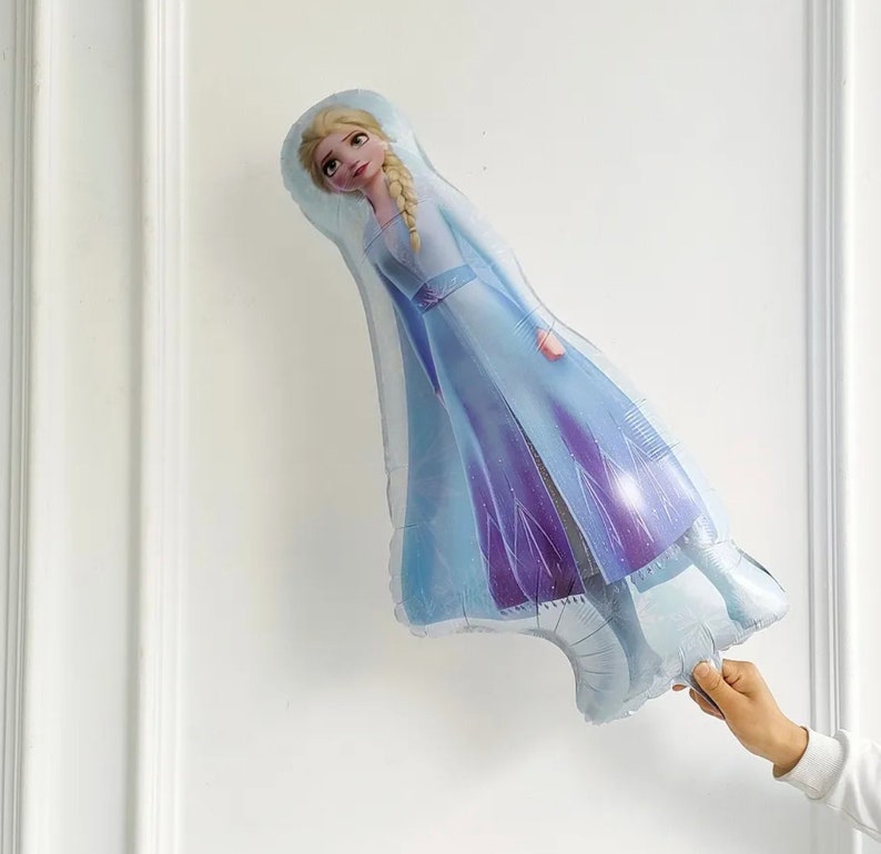 Puede incluir: Un globo de aluminio azul y morado con forma de Elsa de la pel&iacute;cula Frozen. Elsa lleva un vestido azul y morado con una capa blanca. Tiene el pelo largo y rubio y est&aacute; mirando hacia arriba.