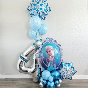 K&ouml;nnte beinhalten: Eine festliche Ballonanordnung mit einer gro&szlig;en silbernen Zahl "4" und einem zentralen Ballon mit einem Prinzessinnenportr&auml;t. Die Anordnung umfasst blaue und silberne Ballons, schneef&ouml;rmige Ballons und kleinere runde Ballons.