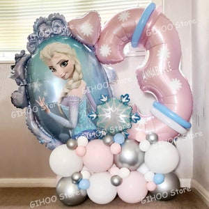K&ouml;nnte beinhalten: Ballonarrangement mit einem gro&szlig;en Elsa-Ballon, einem Ballon mit der Zahl 3 und verschiedenen kleineren Ballons in Wei&szlig;, Rosa und Silber. Der Ballon mit der Zahl 3 tr&auml;gt den Namen "ANNABELLE". Schneeflocken-Akzente sind sichtbar.