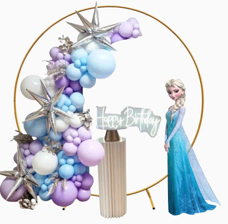 Puede incluir: Un arco de metal dorado decorado con una cascada de globos morados, azules y blancos. Un soporte para pastel blanco con un letrero que dice "Happy Birthday" est&aacute; frente al arco. Una figura de una ni&ntilde;a con un vestido azul se encuentra a la derecha del arco.