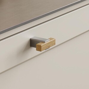 May include: Close-up of a kitchen cabinet with a stainless steel countertop and a light wood and metal drawer pull. The cabinet door is a light cream colour. A bottle of oil and a marble mortar are visible in the background.