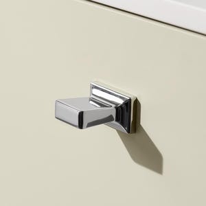 May include: A cream-coloured cabinet door with a chrome square handle. The handle is mounted on the door and casts a shadow. The top of the cabinet has a white countertop.