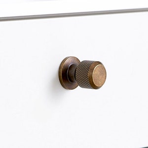 May include: Two white drawers with brass knobs. The knobs have a textured, knurled design.