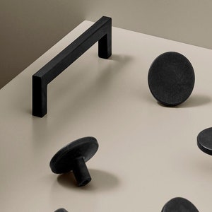 May include: A set of black cabinet hardware, including a bar pull and round knobs. The hardware has a matt finish.