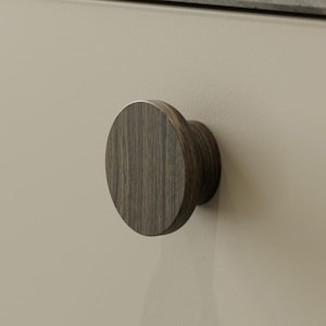 May include: A wooden cabinet knob with a circular face and a cylindrical base. The knob is a dark brown colour with visible wood grain. It is mounted on a light beige cabinet door.