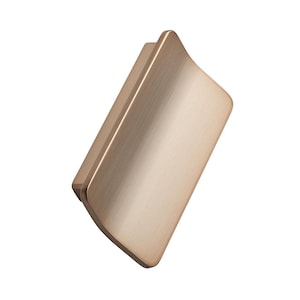 May include: A brushed gold cabinet pull with a curved design. The hardware is rectangular with a slightly rounded edge, and is designed to be mounted horizontally. The pull has a smooth, matte finish.