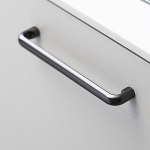 May include: A brushed nickel cabinet pull with rounded edges.
