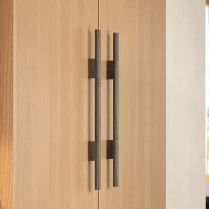 May include: Two black metal cabinet pulls with a brushed finish. The pulls are mounted on a light wood cabinet door.