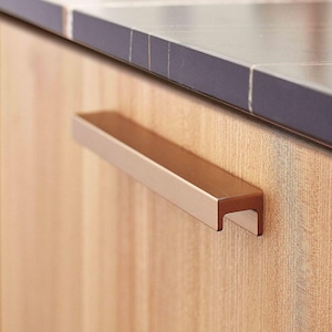 May include: A brushed nickel cabinet pull with a rectangular shape and a slight curve at the top. The pull is mounted on a light wood cabinet door.