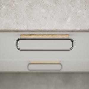 May include: Close-up of a white cabinet with a marble countertop. The cabinet features a rectangular, dark grey handle with a wooden accent. The handle is approximately 25 cm long. The design is modern and minimalist.