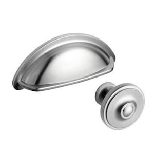 May include: A pair of brushed nickel cabinet hardware items. One is a cup pull with a curved shape, and the other is a round knob. Both have a matte finish and are designed for furniture applications.