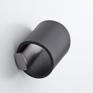 May include: A dark grey bottle stopper with a cylindrical leather sleeve. The stopper has a textured surface and a grey, angled handle. The design is simple and modern, suitable for wine bottles.