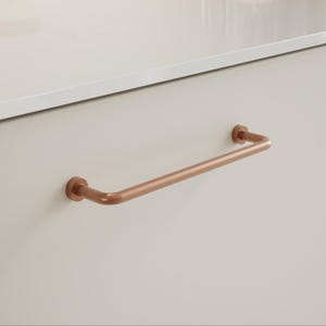 May include: A copper-coloured towel rail fixed to a light beige surface. The rail is a rounded, horizontal design with circular mounting plates. The style is modern and minimalist, suitable for a bathroom or kitchen.
