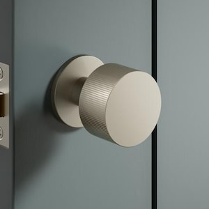 May include: A close-up of a door knob and lock set. The door knob is a cylindrical shape with a ridged edge and a flat, circular face. The lock set is gold-coloured and mounted on a grey door.