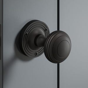 May include: A black door knob with a round, grooved design. The knob is mounted on a dark grey door with a matching black backplate. The door also features a gold-coloured latch.