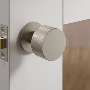 May include: A close-up of a contemporary door handle and lock set. The door handle is cylindrical with a textured surface, and the lock has a gold-coloured latch. The door and frame are white.