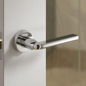 May include: A contemporary chrome door handle and latch set. The handle has a minimalist design and is mounted on a white door. The door is partially open, showing a glass panel and a glimpse of the room beyond.