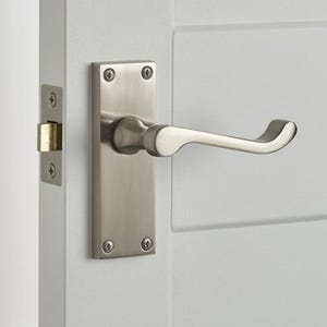 May include: A brushed nickel door handle and plate are mounted on a white door. The handle has a curved design, and the plate is rectangular with four visible screws. The door has horizontal grooves.
