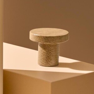 May include: A wooden knob with a textured surface. The knob is light brown in colour and has a round top and a cylindrical base.