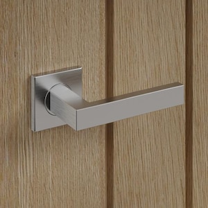 May include: A modern door handle and latch in a close-up shot. The handle is brushed silver, with a square base and a rectangular lever. The door is light brown wood with vertical grain.