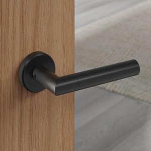 May include: A black door handle with a round base and a straight lever is mounted on a light brown wooden door. The door also features a black strike plate and a gold-coloured latch. The door is part of a modern interior design.