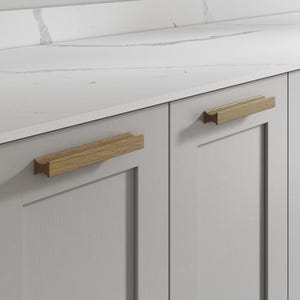 May include: Close-up of a light grey cabinet with two wooden handles. The handles are rectangular with a light brown finish. A white countertop with grey veining is above the cabinet.
