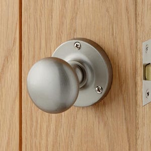 May include: A brushed nickel door knob with a round backplate and a spherical handle is mounted on a light-coloured wooden door. The door also features a matching brushed nickel strike plate and a brass-coloured latch.