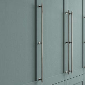 May include: Close-up of a section of a pale blue cabinet with long, brushed nickel bar pulls. The cabinet doors have a vertical wood grain texture. The pulls are mounted with small, round hardware.